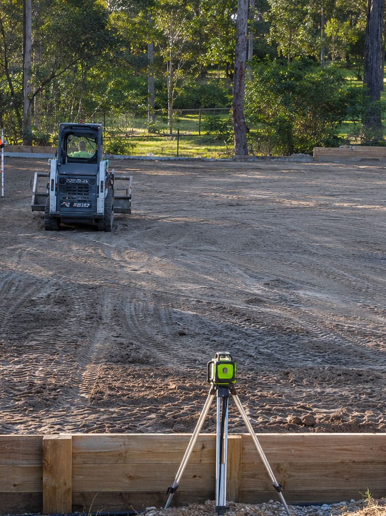 Holly Civil skid-steer leveling a pad framed by timber retaining walls in Jimboomba